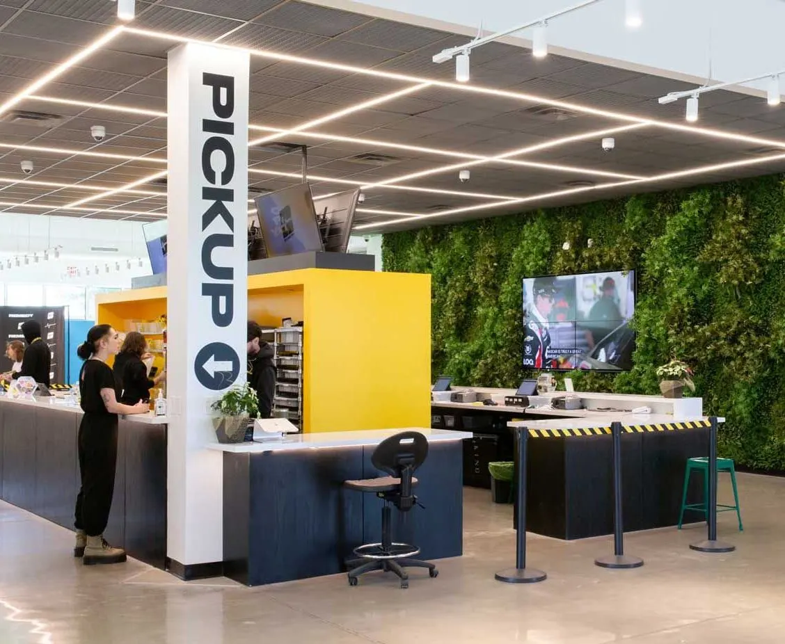 Bright cannabis dispensary interior with pickup counter and green plant wall